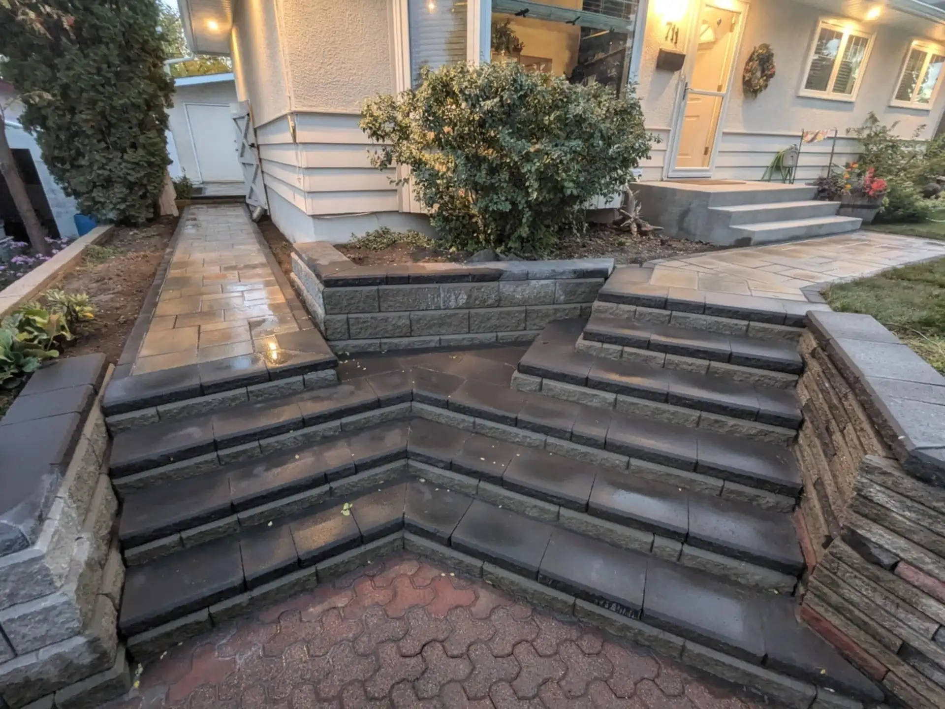 Wide block steps between stacked block retaining walls, leading to a paver walkway and the front door