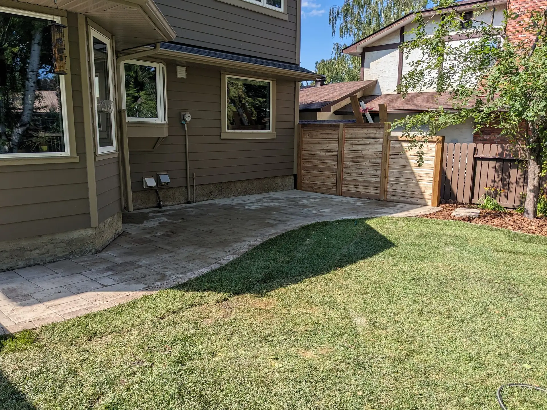 Paver patio along the house with fresh sod and a cedar privacy screen